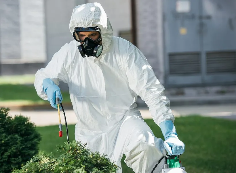 A pest control technician in protective gear spraying outdoors