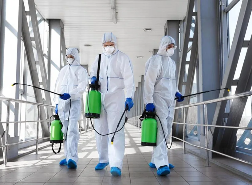 Three technicians in protective coveralls walking with spray equipment